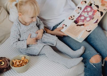 Mother reading a book to her daughter in a cozy bedroom setting with snacks nearby.