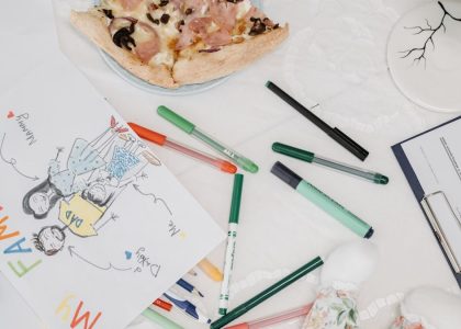 A colorful child's drawing of a family alongside pizza and pens on a table.